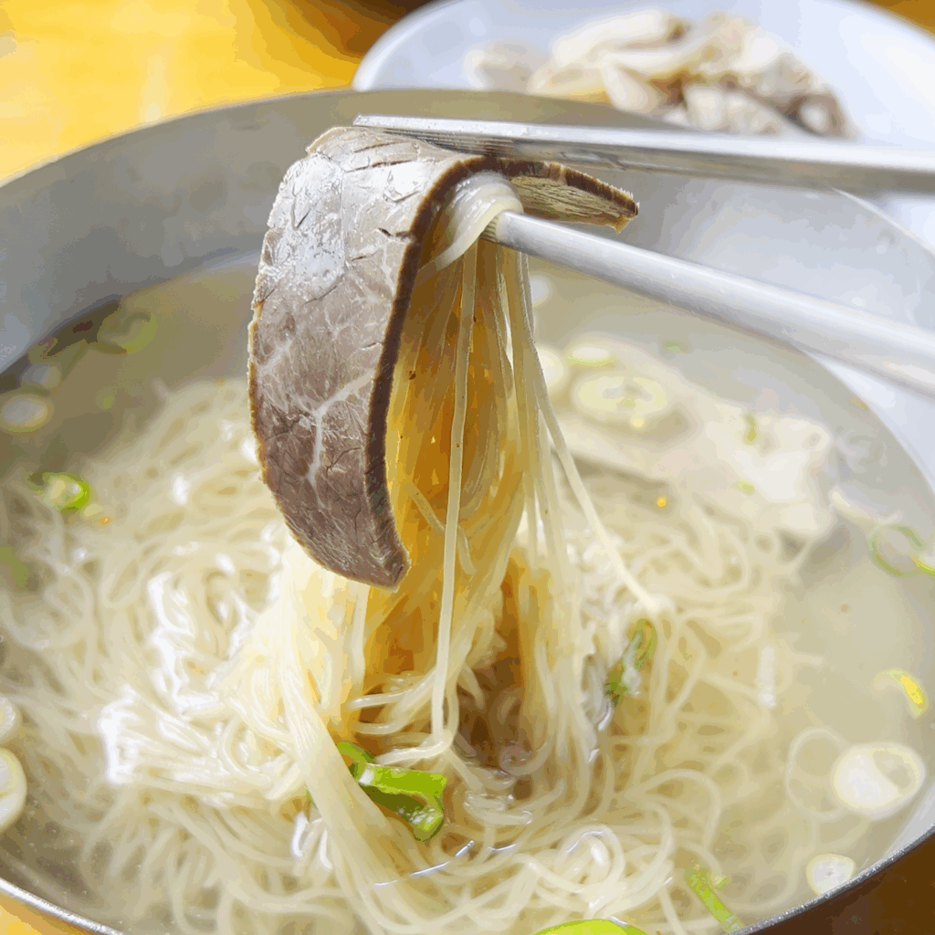 젓가락으로 필동면옥 평양냉면의 메밀면과 수육을 함께 들어올리는 모습