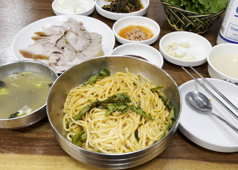 대선칼국수의 비빔칼국수와 함께 수육, 막걸리, 국물, 기본 반찬이 모두 차려진 전체 상차림. A full table setting at Daeseon Kalguksu, featuring bibim-kalguksu, suyuk, makgeolli, and various side dishes.