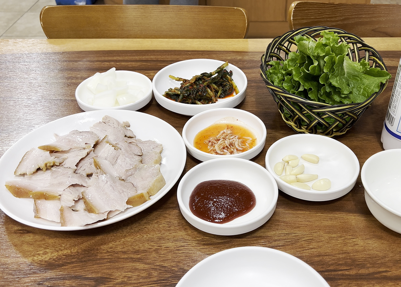 돼지고기 수육과 함께 쌈을 싸먹을 수 있도록 상추, 마늘, 쌈장, 새우젓 등이 함께 나온 상차림. A full table setting for suyuk ssam (pork wraps), including lettuce, garlic, ssamjang, and salted shrimp.