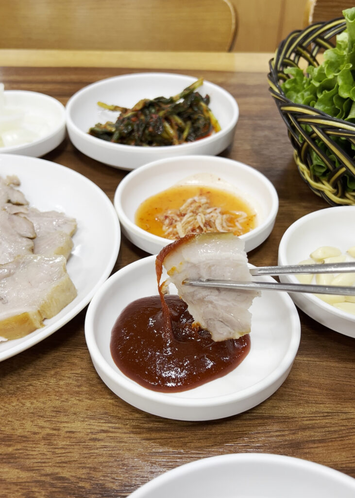 젓가락으로 집은 수육 한 점을 쌈장에 찍는 모습. Dipping a piece of boiled pork suyuk into ssamjang (Korean spicy dipping sauce) with chopsticks.