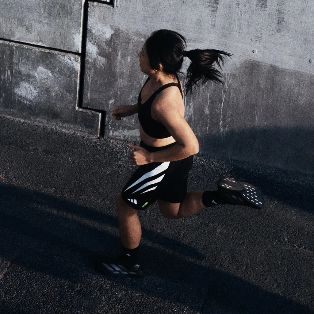 아디다스 아디제로 에보 SL 블랙 러닝화를 신고 야외에서 달리는 여성 러너의 역동적인 모습. 런린이 훈련, 아디다스 러닝 복장. Dynamic shot of a female runner wearing black Adidas Adizero Evo SL running shoes during an outdoor run. Beginner runner training, Adidas running attire.