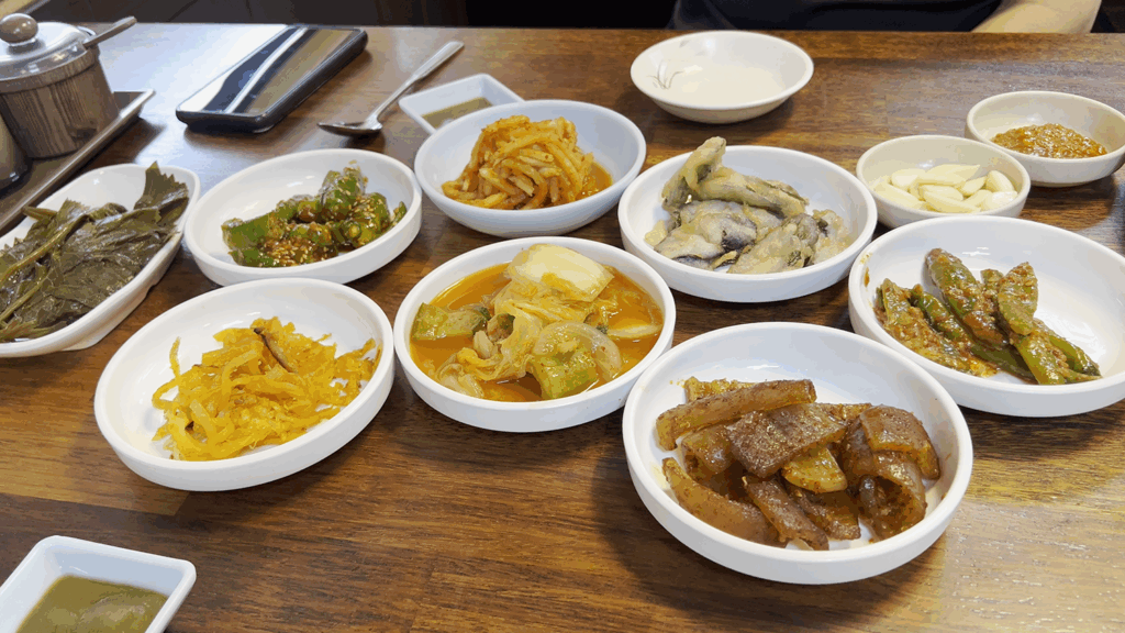 정갈하게 차려진 광천식당의 다양한 밑반찬들. 김치, 장아찌, 무생채 등이 보인다. A wide variety of Korean side dishes (banchan) served at Gwangcheon Sikdang in small white bowls.