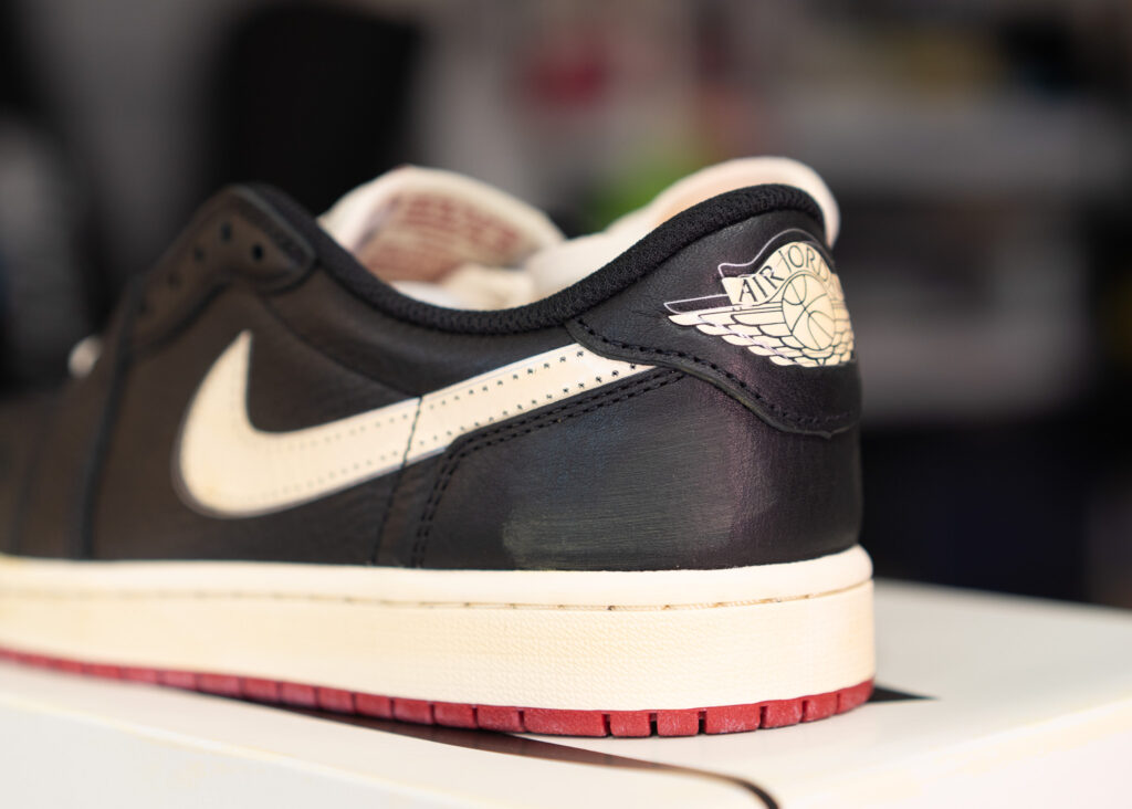 나이젤 실베스터 조던 1 로우 힐카운터의 에어 조던 윙스 로고와 크랙 레더 디테일. The Air Jordan Wings logo and cracked leather detail on the heel counter of the Nigel Sylvester Jordan 1 Low.