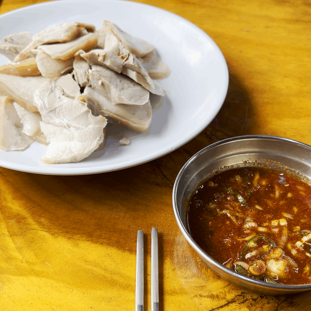 A close-up shot of a white plate filled with thinly sliced, tender jeyuk (boiled pork) at Pildong Myeonok.