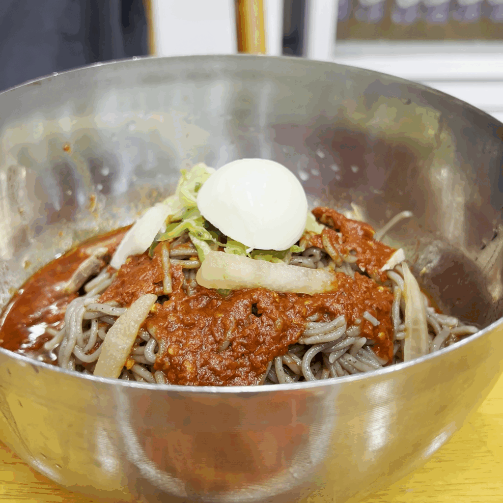삶은 계란 반쪽이 올라가 있는 평남면옥의 비빔냉면 한 그릇. A full bowl of bibim-naengmyeon at Pyeongnam Myeonok, topped with a hard-boiled egg.