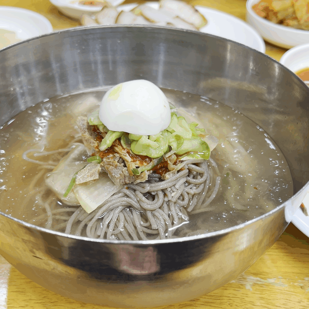 시원한 동치미 국물에 메밀면과 고명이 담겨 나오는 평남면옥의 물냉면. A bowl of Pyeongnam Myeonok's mul-naengmyeon (cold noodle soup) with buckwheat noodles in a clear dongchimi broth.