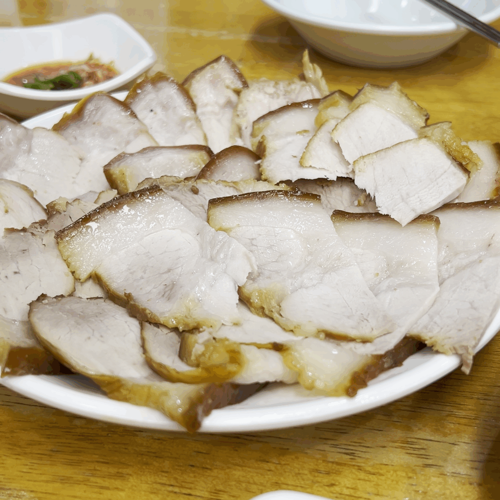 흰 접시에 먹음직스럽게 담겨 나온 평남면옥의 대표 메뉴, 돼지고기 편육. A platter of Pyeongnam Myeonok's signature pork pyeonyuk (boiled pork slices) served on a white dish.