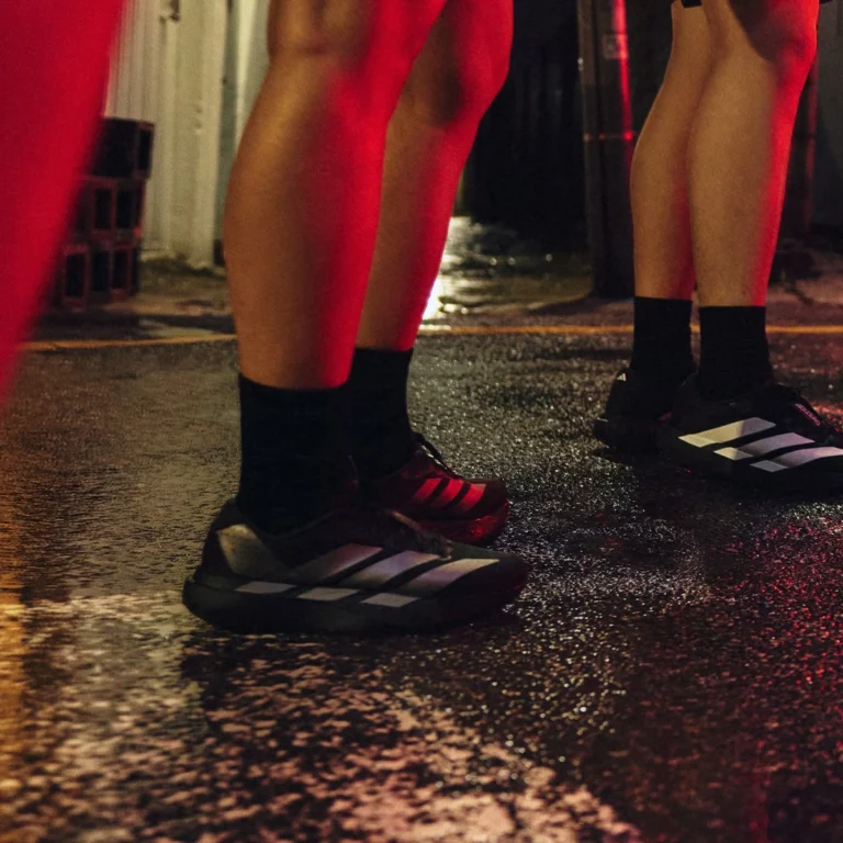 한글 대체 텍스트: 비 오는 밤거리, 아디다스 아디제로 에보 SL (블랙)과 아디다스 러닝화 (레드)를 신은 두 러너의 발. 야간 러닝, 러닝화 접지력. Feet of two runners wearing Adidas Adizero Evo SL (black) and Adidas running shoes (red) on a wet street at night. Night running, running shoe grip.