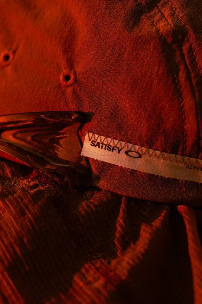 새티스파이와 오클리 로고가 함께 있는 협업 직조 라벨 디테일. A detail shot of the woven collaboration label featuring both the Satisfy and Oakley logos.