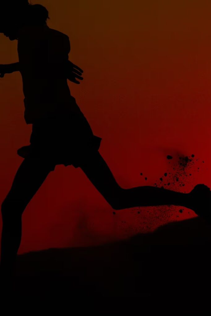 붉은 배경 속에서 역동적으로 달리는 러너의 실루엣. The silhouette of a runner in dynamic motion against a red gradient background.