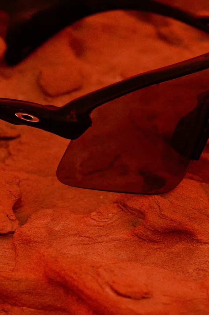 붉은 돌 위에 놓인 오클리 '스턴트 데빌' 선글라스의 측면 클로즈업. A side profile close-up of the Oakley 'Stunt Devil' sunglasses on a red rock.