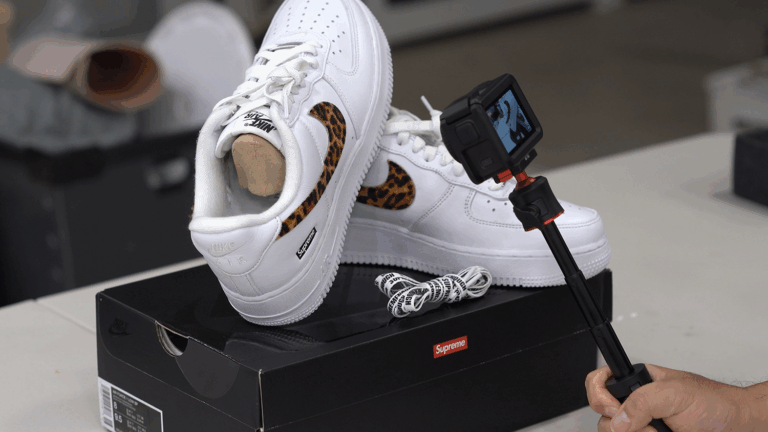검정색 나이키 박스 위에 놓인 슈프림 x 굿이너프 에어 포스 1 스니커즈와 여분 신발끈. The Supreme x Goodenough Air Force 1 sneakers with extra laces, displayed on top of their black Nike box.