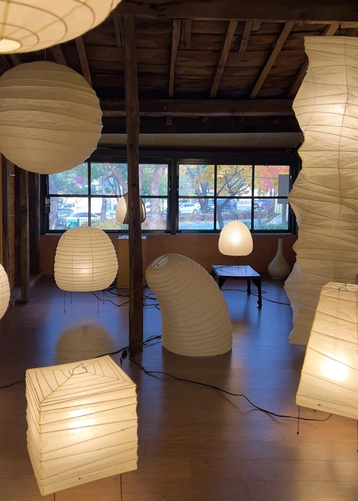 다양한 종이 조형 형태의 아카리 조명이 설치된 공간 전경 Wide view of diverse paper Akari light forms installed in the exhibition