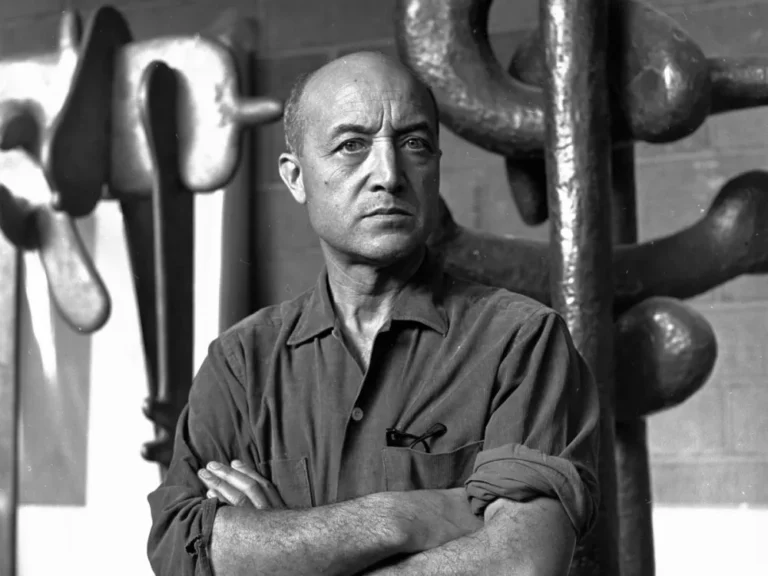 조각 작품들을 배경으로 팔짱을 끼고 서 있는 이사무 노구치 Isamu Noguchi standing with arms crossed in front of sculptural works