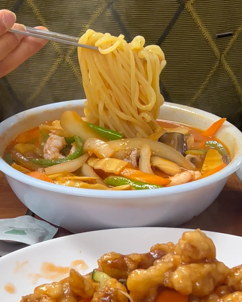젓가락으로 하림각 짬뽕의 탱글탱글한 면발을 한가득 들어 올리고 있는 모습. Chopsticks lifting a large portion of chewy noodles from a bowl of Harimgak's spicy jjamppong.