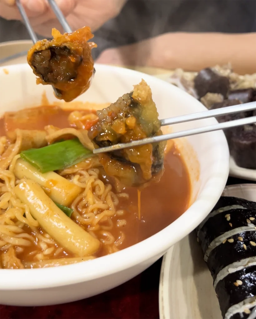 김말이 튀김을 라볶이 국물에 찍는 장면 Fried seaweed roll dipped in spicy rabokki sauce at Saeam Bunsik