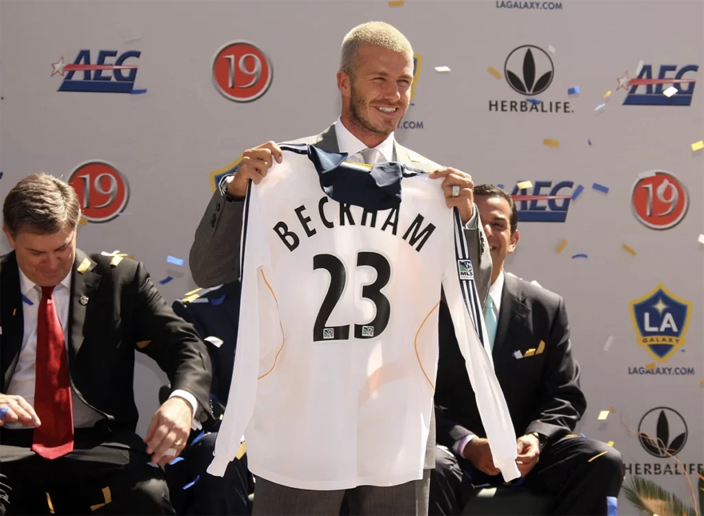 데이비드 베컴이 LA 갤럭시 입단을 발표하며 MLS 유니폼을 들고 있는 모습 David Beckham holding an LA Galaxy jersey during his MLS signing announcement